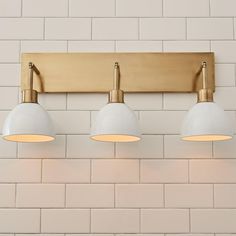 three lights are mounted on the wall in front of a white brick wall with gold trim