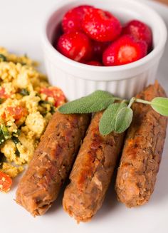 sausages, scrambled eggs and strawberries on a white plate with green leafy garnish