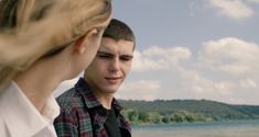 a young man and woman standing next to each other near the water's edge