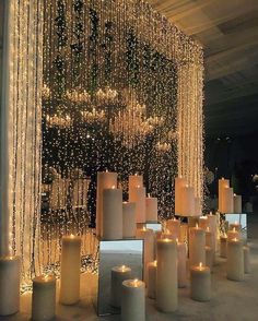 many candles are lit up in front of a wall with beads and lights on it