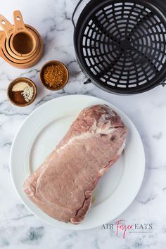 raw pork on a plate with spices and seasonings next to it, including an air fryer