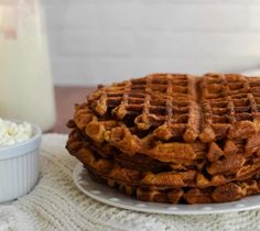 a stack of waffles sitting on top of a white plate next to a glass of milk