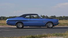 an old blue car is parked on the side of the road in front of some grass