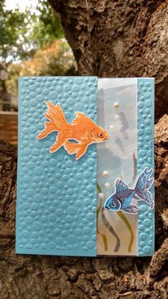 a card with an orange fish on it and blue paper in front of a tree