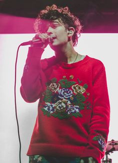 a young man singing into a microphone while wearing a red sweater with flowers on it