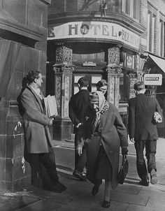 an old black and white photo of people walking in front of a building with a sign on it