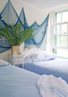 two beds in a room with blue bedding and white walls, one has a fish net on the headboard