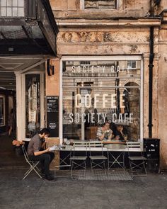 two people sitting at tables in front of a cafe