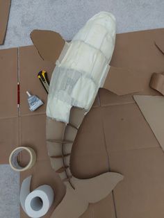 the cardboard shark is laying on the floor next to tape and construction supplies, along with other items