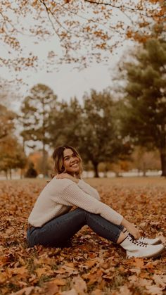 a woman sitting on the ground surrounded by leaves