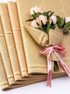 three folded newspapers with flowers on them and ribbon tied around the edges, sitting next to each other