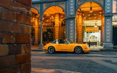 a yellow sports car parked in front of a building with lights on it's windows