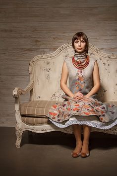 a woman sitting on top of a white couch in front of a wooden wall behind her