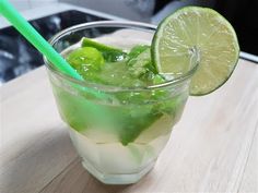 a glass filled with ice and limeade on top of a wooden table next to a green straw