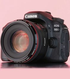 a canon camera sitting on top of a pink surface with the lens up close to it's body