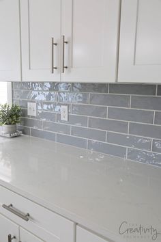 a kitchen counter with white cabinets and gray tile backsplashes on the wall