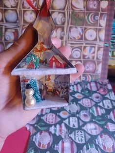 a hand holding a small house ornament in front of a wall covered with christmas ornaments