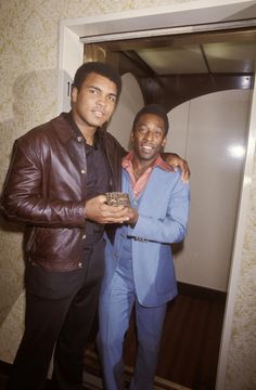 two men standing next to each other in front of a mirror and smiling at the camera