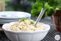 a white bowl filled with macaroni salad on top of a table next to plates