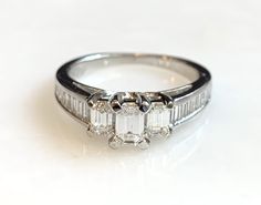 Here is a beautiful 14k white gold emerald cut diamond ring. The center stone is .20ct. with 2 side emerald cut diamonds totaling .30ct. There are also 16 baguettes in the band totaling .56ct. A beauty that will get a lot of compliments! Metal: 14K White Gold Diamonds: 1-Emerald Cut .20cttw, 2-Emerald cut .30cttw, G/H, VS, 16-side stones .56cttw, Weight: 3.8 grans Size: 6.5 SKU# 21SB080619 If you have any questions on this item, please message us! GandDJewelers.etsy.com Please note that all of o Diamond White Emerald Cut Emerald Ring With Diamond Accents, Emerald Cut Diamond White Emerald Ring With Diamond Accents, Gia Certified Emerald Cut Diamond Ring In Diamond White, White Emerald Ring With Diamond Accents, Emerald Cut Platinum Wedding Ring In Diamond White, Fine Jewelry Emerald Cut Diamond Ring With Baguette Diamonds, Modern Gia Certified Emerald Cut Diamond Ring, White Emerald Cut Platinum Diamond Ring, 14k White Gold Emerald-cut Diamond Ring