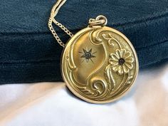 Description: Lovely antique Art Nouveau gold filled photo locket on a 14K gold filled chain. The front features an ornate repousse design with flowers and some leafy and curling designs on the bottom edge and two round faceted paste (glass) gems. The locket hangs on a new 14K gold filled curb chain with a spring ring clasp.  On the locket front top left section is an etched starburst shape that has a clear paste gem set inside it. On the right bottom side is a raised ten-petaled flower with a wonderful Repousse curled stem. The flower is set with a pink paste gem in the center. The flower and its stem along with some other decorative swirls fill up and curl around the bottom of the locket and create a lovely contrast to the starburst on a satin background on the opposite / top left side. Gold Medallion Locket Necklace Stamped 14k, Antique Medallion Locket Necklace Stamped 14k, Antique Gold Locket Necklace Stamped 14k, Victorian Round Locket Necklace Stamped 14k, Antique Gold Keepsake Pendant Jewelry, Antique Gold Pendant Jewelry For Keepsake, Victorian Yellow Gold Pendant Locket Necklace, Victorian Yellow Gold Locket Necklace For Formal Occasions, Victorian Filigree Locket Necklace In Yellow Gold