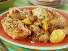 a red plate topped with chicken and lemons on top of a green table cloth