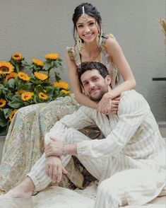 a woman sitting on the back of a man's lap with sunflowers in the background