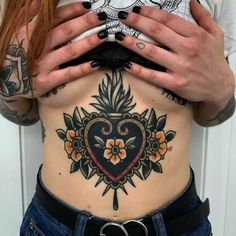 a woman with tattoos on her stomach holding up her hands to her chest and looking at the camera