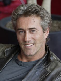 a close up of a person wearing a leather jacket and smiling at the camera with a pot in the background