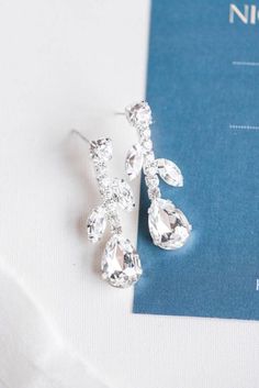 a pair of crystal earrings sitting on top of a blue and white paper next to a card