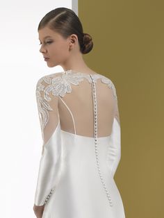 a woman wearing a white dress with long sleeves and beaded details on the back