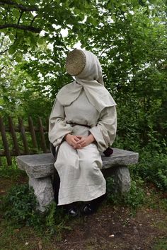 a woman sitting on top of a bench covered in a blanket and covering herself with her hands