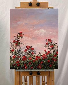 an easel with a painting on it that has red flowers in the foreground