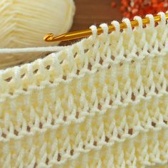 a close up view of a crochet stitch with yarn and knitting needles in the background