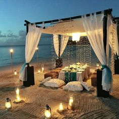 an outdoor dinner setup on the beach with candles lit up for guests to eat and drink