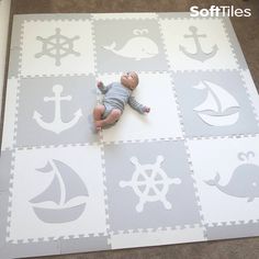 a baby laying on top of a white and gray rug with anchors, whale, boat, and ship wheel stencils