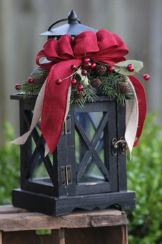 a small lantern with a red bow and pine cones on the top is sitting on a wooden table