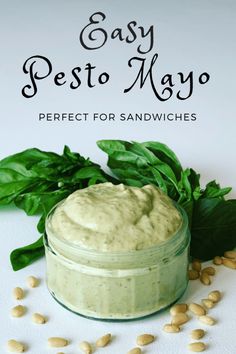 a jar filled with pesto mayo next to some basil leaves