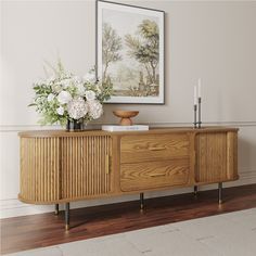 a sideboard with flowers and candles on it in front of a framed art piece