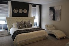 a white bed sitting in a bedroom next to a window filled with curtains and pillows