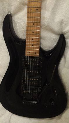 a black electric guitar laying on top of a white sheet with its strings down and the neck up