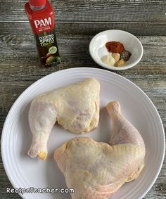 two raw chicken legs on a white plate with spices and seasoning next to it