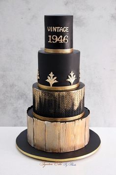 a three tiered black and gold birthday cake with an aged wood design on top