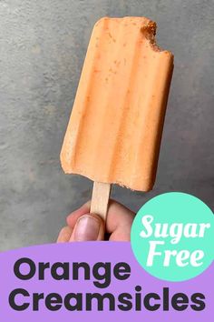 a hand holding an orange ice cream on a stick with the text sugar free orange ice creamsices