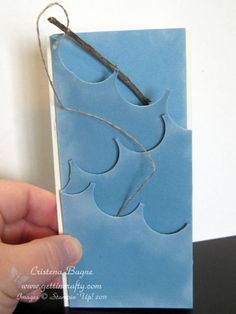 a hand holding a piece of blue paper with scissors in it and string attached to it