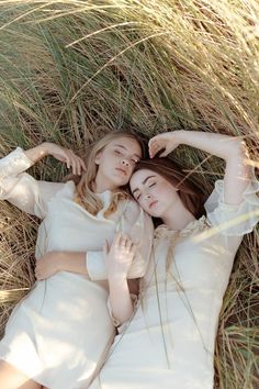 two young women laying in the grass with their arms around each other's shoulders