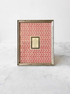 a pink and silver frame with a gold border around the edges on a marble surface