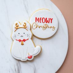 two decorated cookies sitting on top of a white marble plate with merry christmas written on it