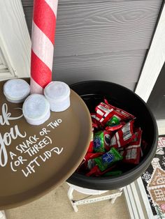 a bucket filled with candy sitting on top of a wooden floor next to a red and white striped pole