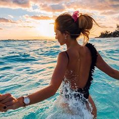 a woman standing in the ocean with her arms out to touch another person's hand